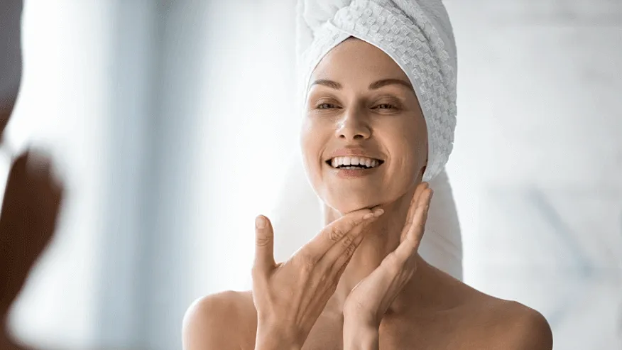Woman applying skincare in bathroom mirror.