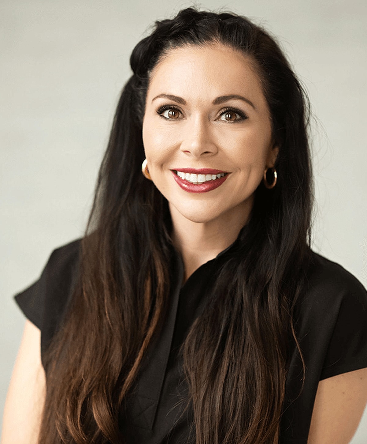 Smiling woman with long dark hair, light background.