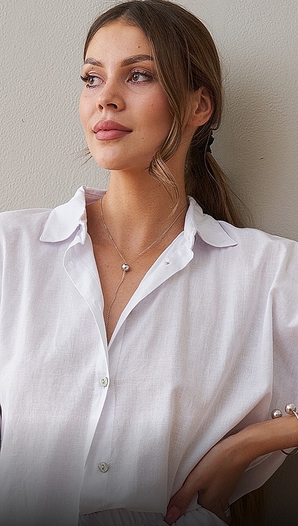 Woman in white shirt with necklace and earrings.