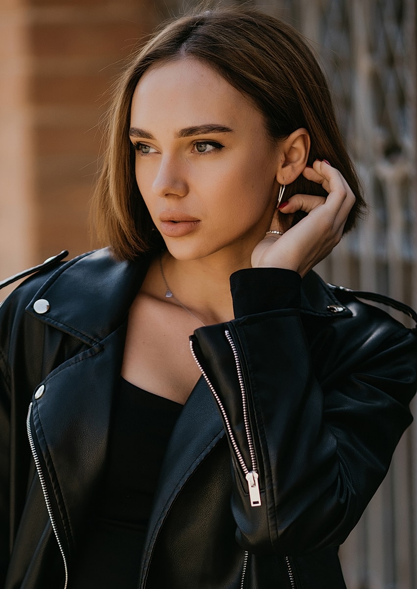 Woman in black leather jacket posing thoughtfully.