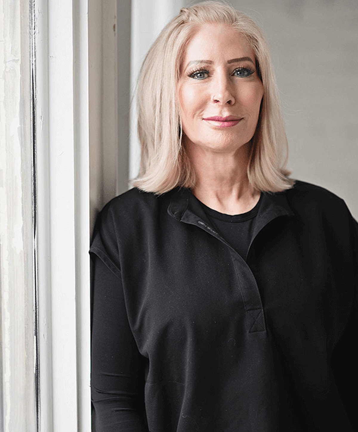 Woman in black attire standing by a window.