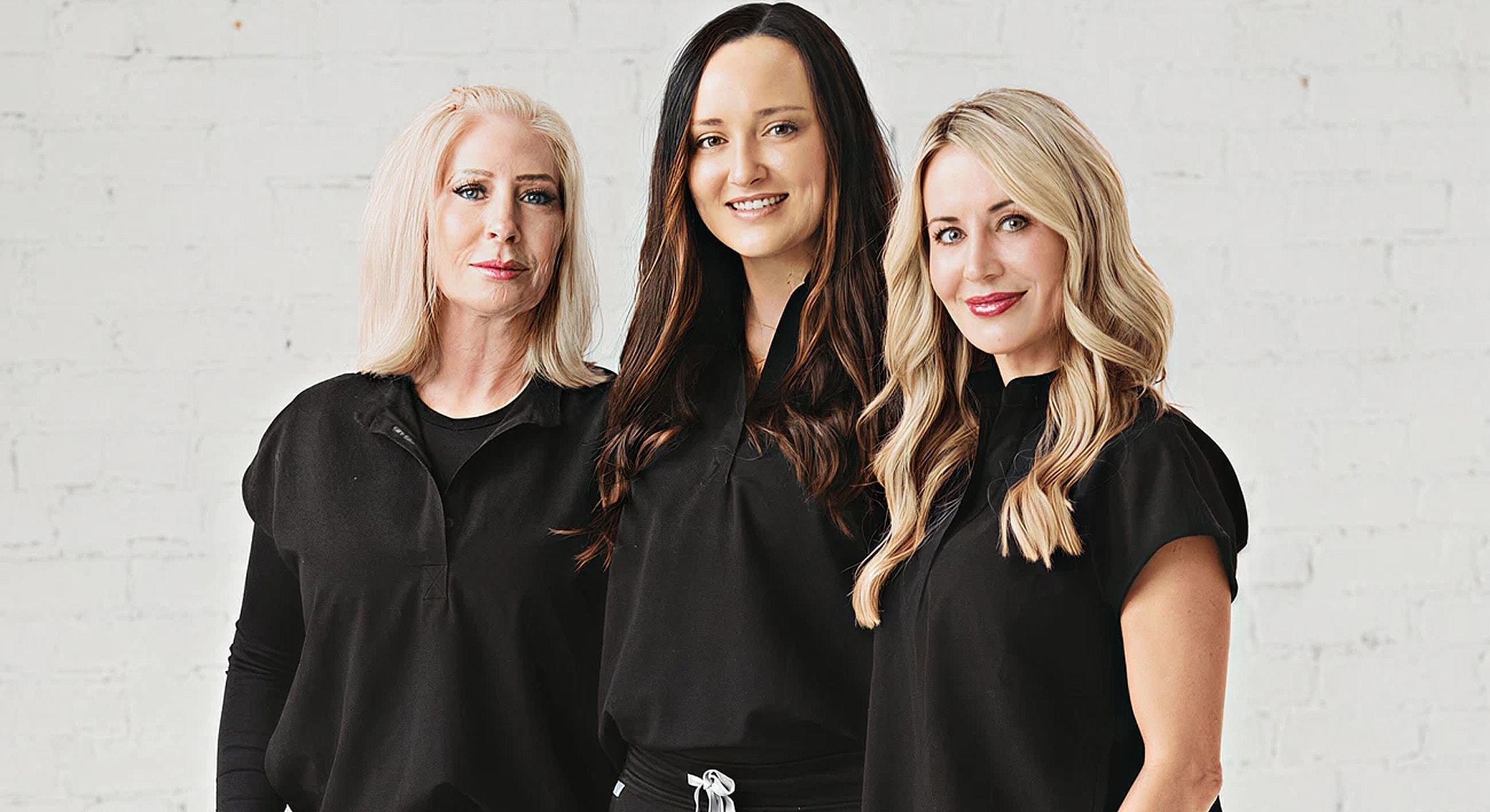 Three women smiling in matching black outfits.