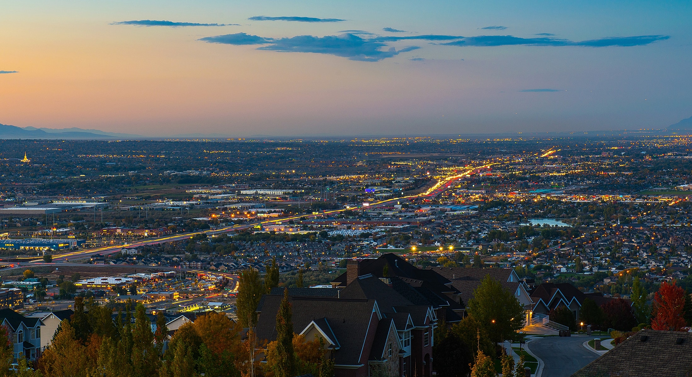 Cityscape at dusk with glowing lights and hills.