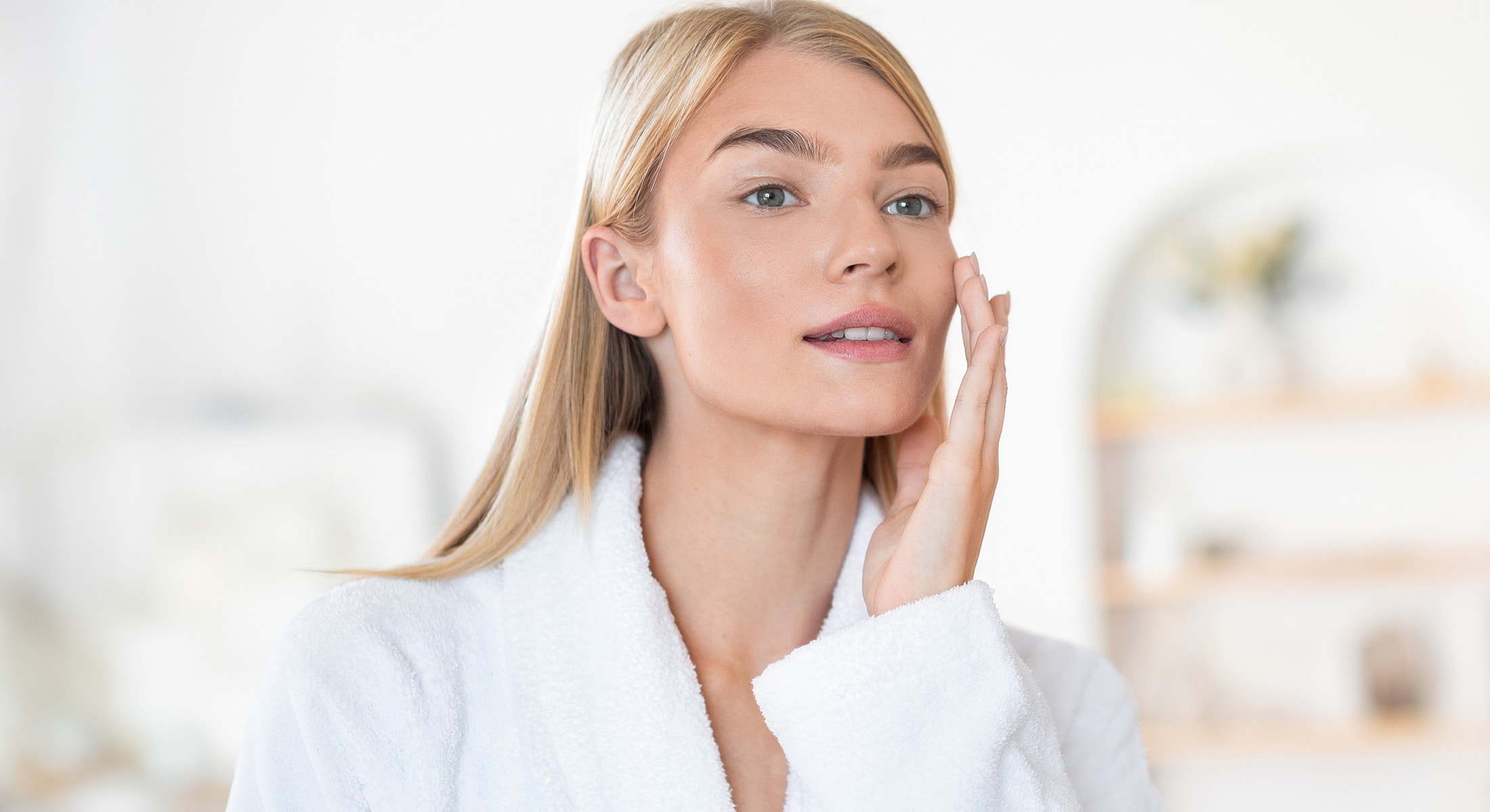 Woman applying skincare in a bright space.